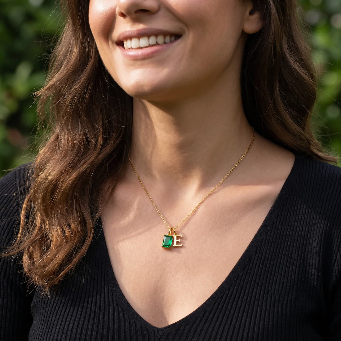 Woman wearing a green rectangular birthstone and uppercase E initial necklace with a black top