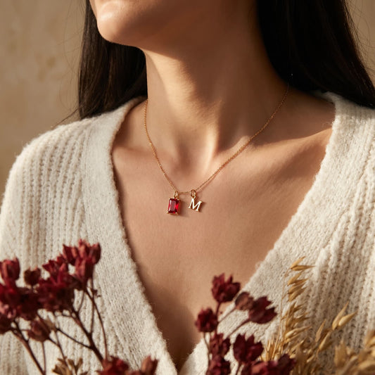Woman wearing a red rectangular birthstone and uppercase M initial necklace with a cream cardigan