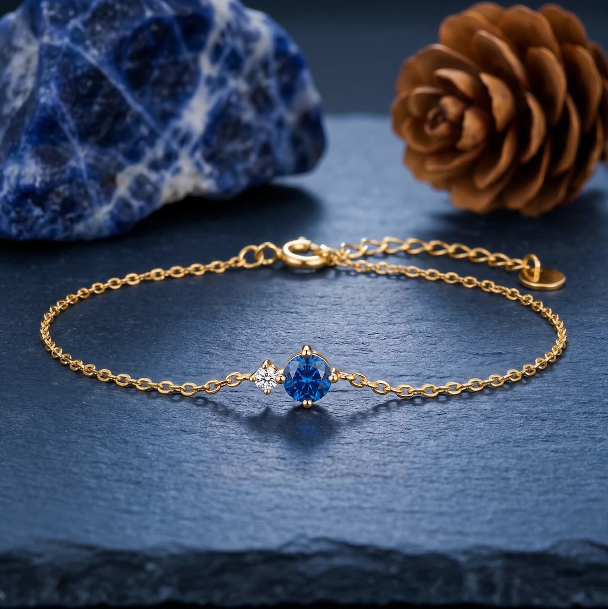 Gold-tone bracelet with a blue round birthstone and clear side accent on a dark stone surface