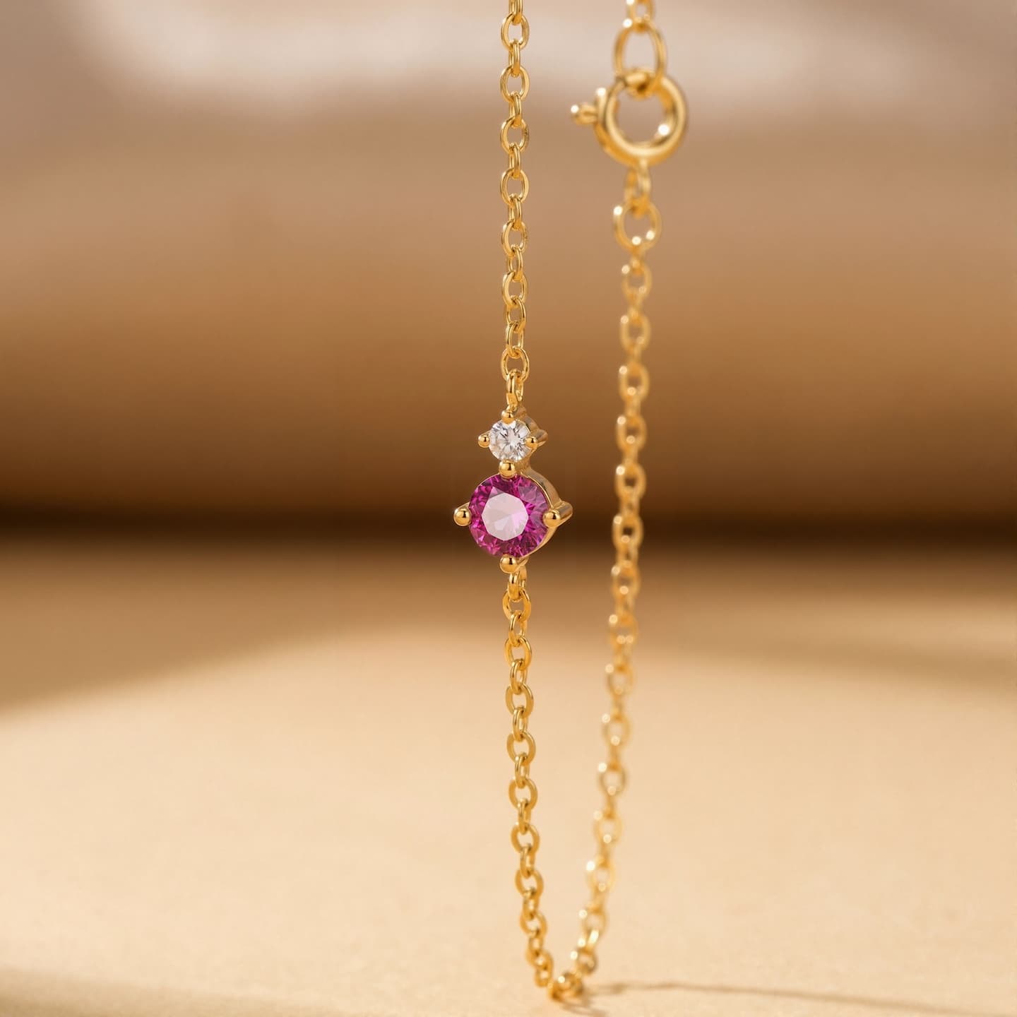 Pink round birthstone bracelet with a clear side accent hanging against a warm neutral background