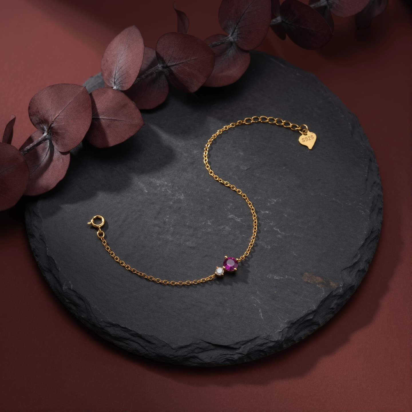 Gold-tone bracelet with a pink round birthstone, clear side accent, and spring-ring clasp on a dark round surface