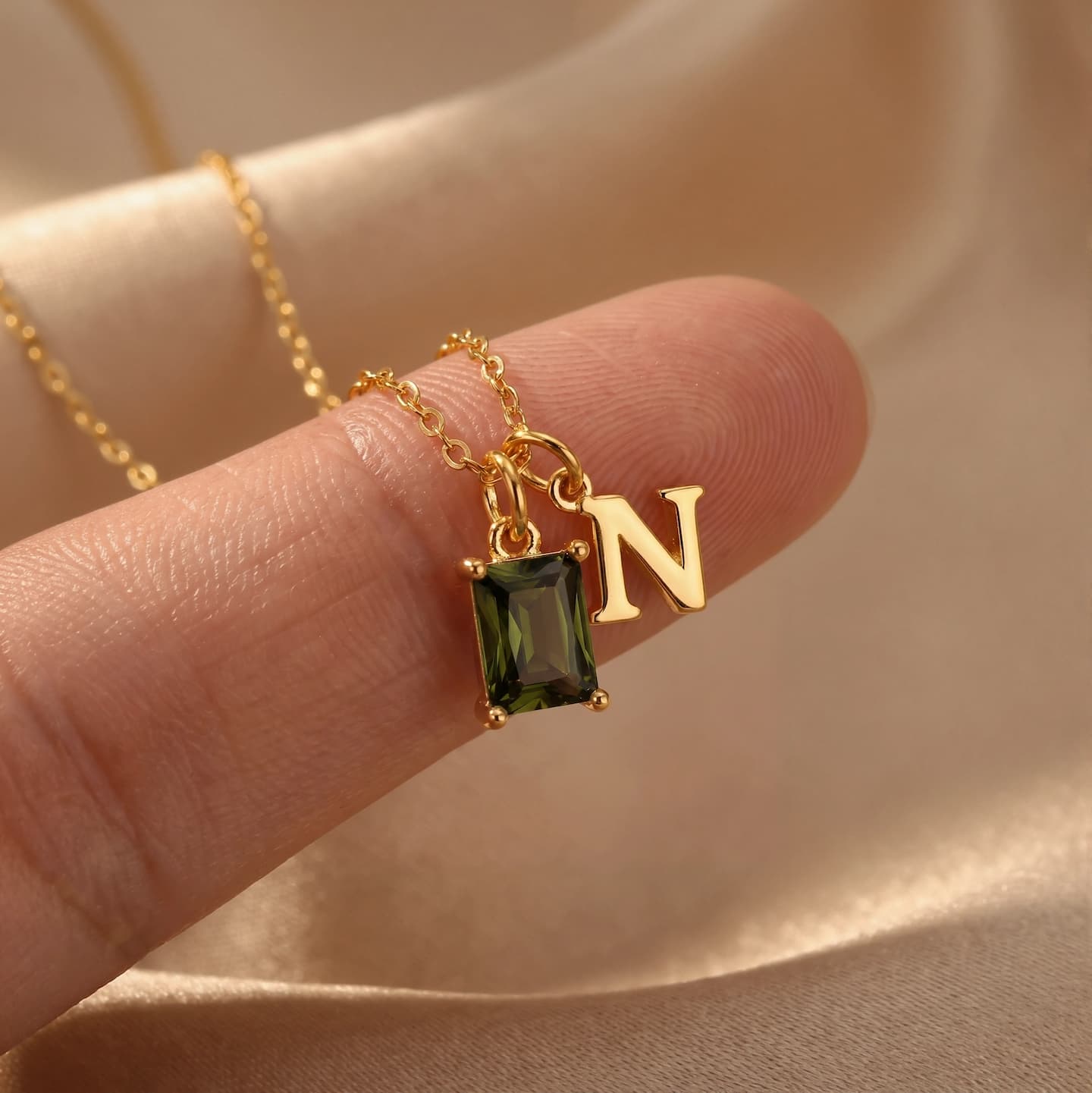 Close-up of an olive-green rectangular birthstone and uppercase N initial held between fingers