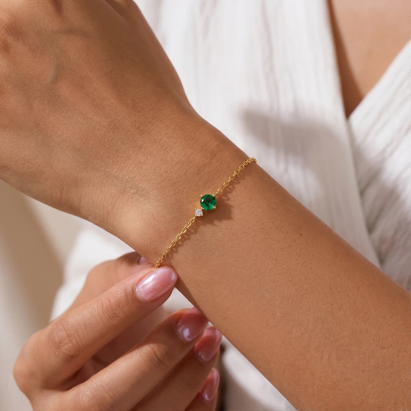 Woman wearing a green round birthstone bracelet with a clear side accent and white sleeveless top