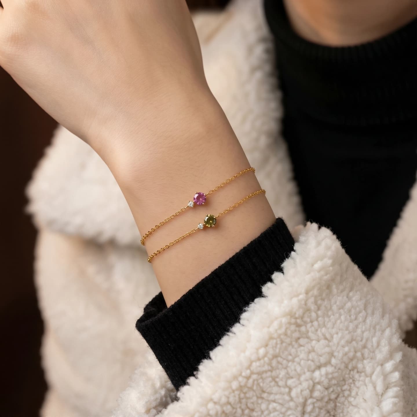 Woman wearing pink and olive-green birthstone bracelets with a black sweater and cream jacket