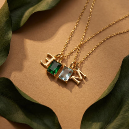 Two gold-tone birthstone necklaces with uppercase E and N initials styled with green leaves