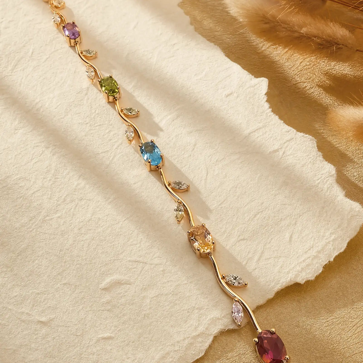 Gold-tone vine bracelet with colorful oval stones on cream paper and warm fabric