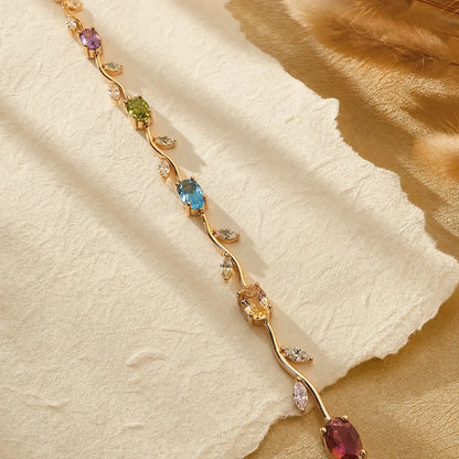 Gold-tone vine bracelet with colorful oval stones on cream paper and warm fabric