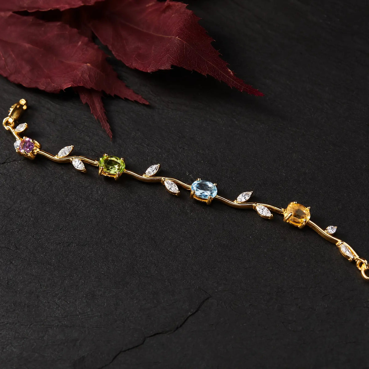 Close view of colorful stones and leaf-shaped accents along a gold-tone vine bracelet