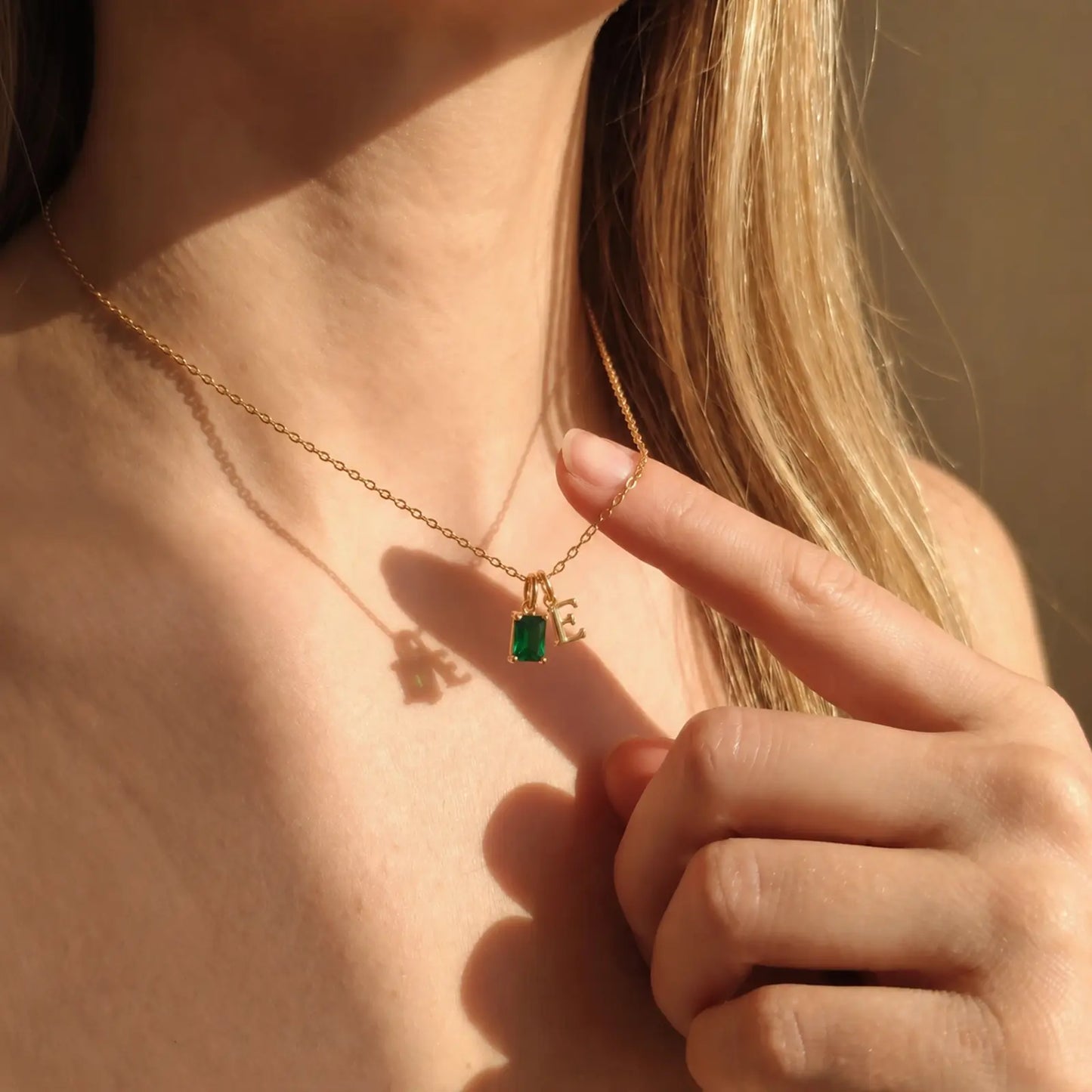Close-up of a green rectangular birthstone and initial necklace in golden hour light