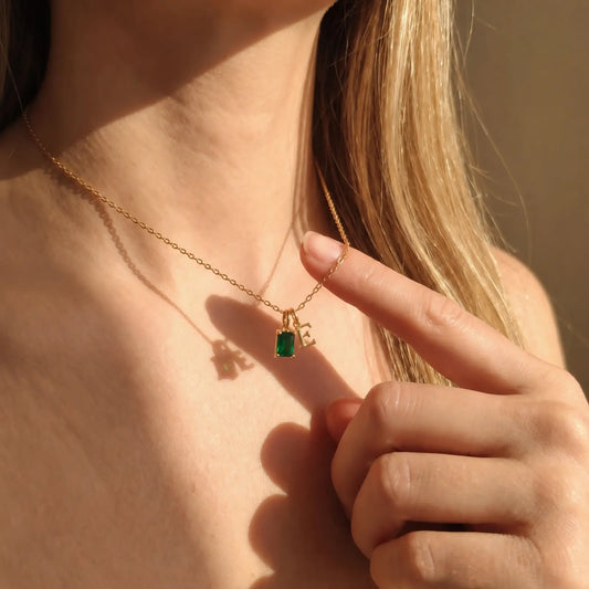 Close-up of a green rectangular birthstone and initial necklace in golden hour light