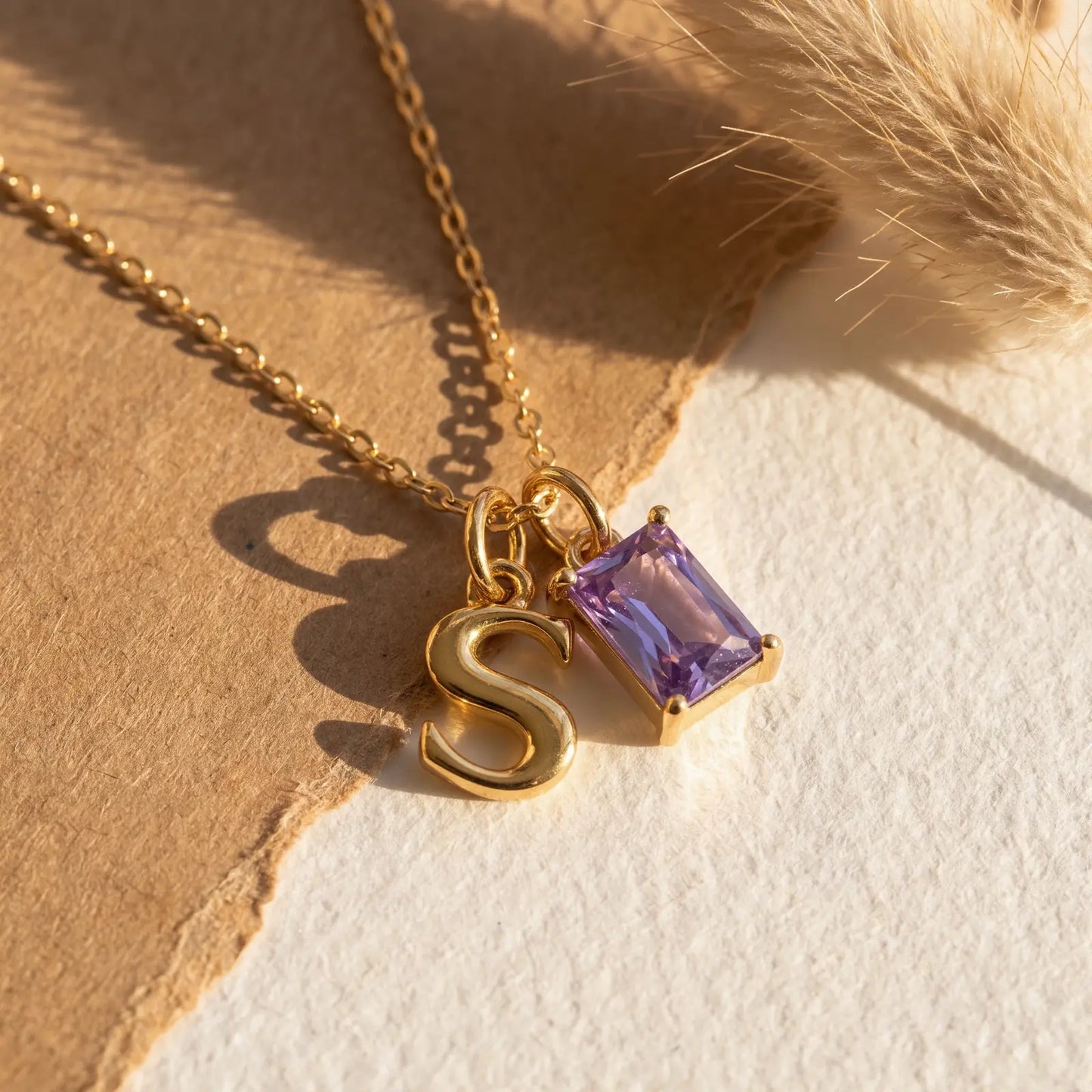 Purple rectangular birthstone and initial necklace on layered natural fabric