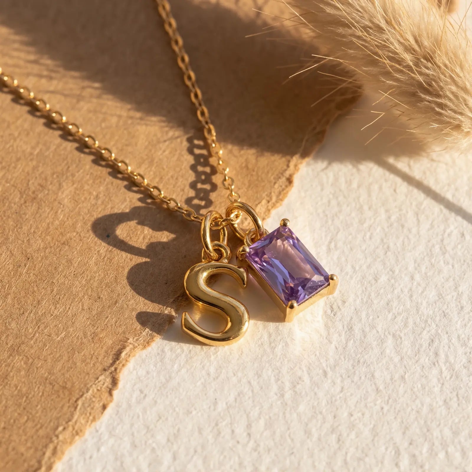 Purple rectangular birthstone and initial necklace on layered natural fabric