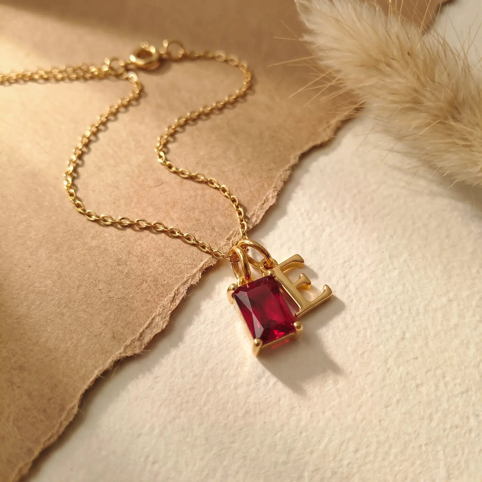 Red rectangular birthstone and initial necklace on layered natural fabric