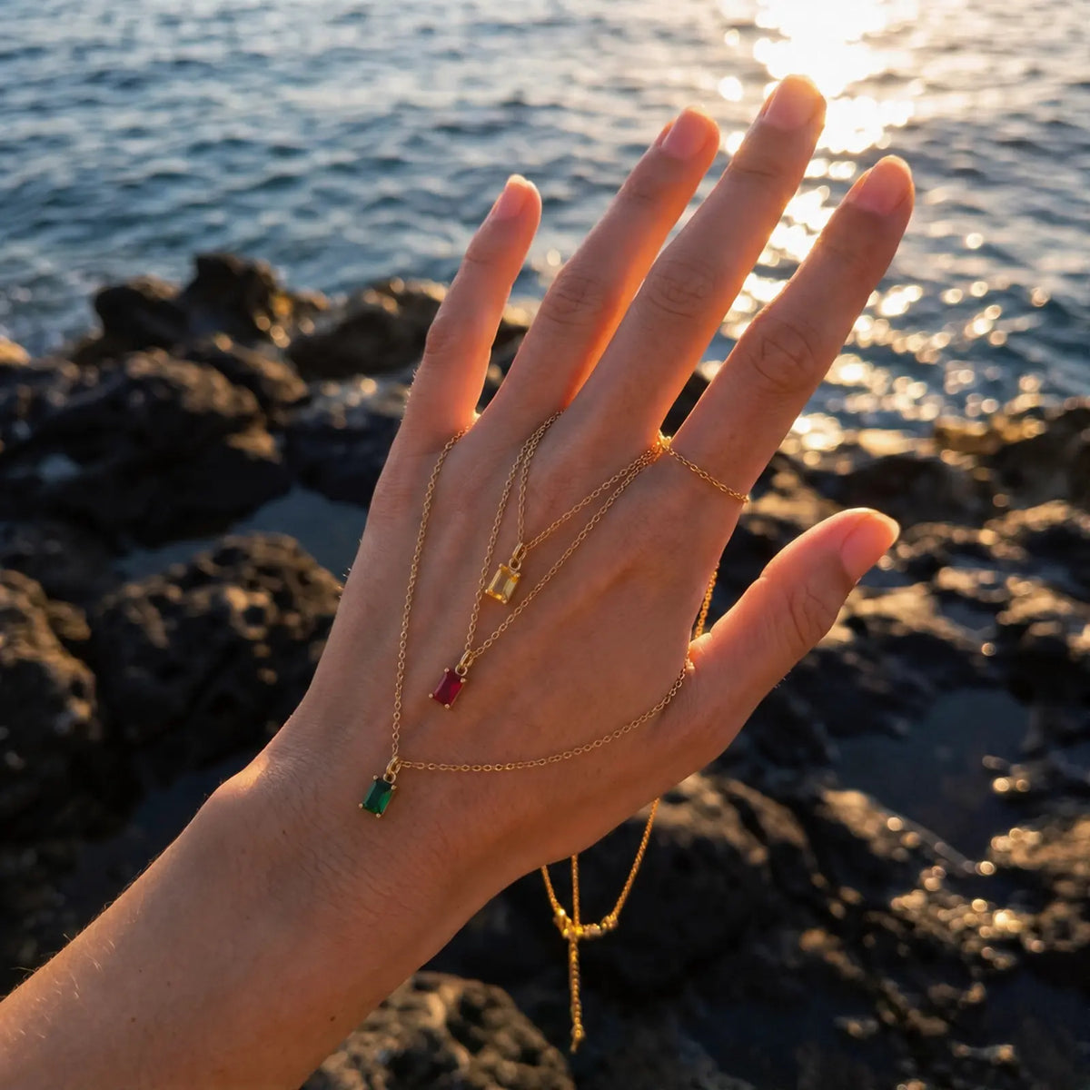 Hand holding a green rectangular birthstone pendant necklace beside the sea
