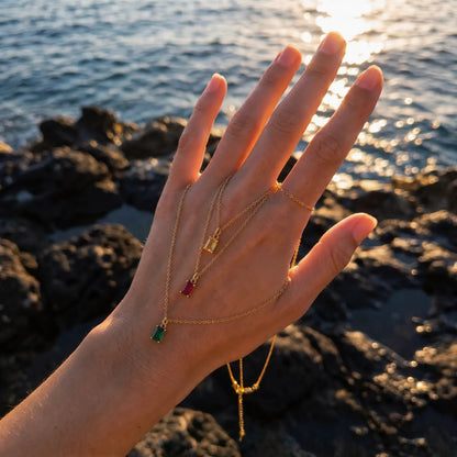 Hand holding a green rectangular birthstone pendant necklace beside the sea