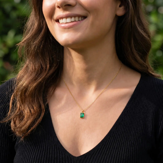 Woman wearing a green rectangular birthstone pendant necklace with a black V-neck knit top