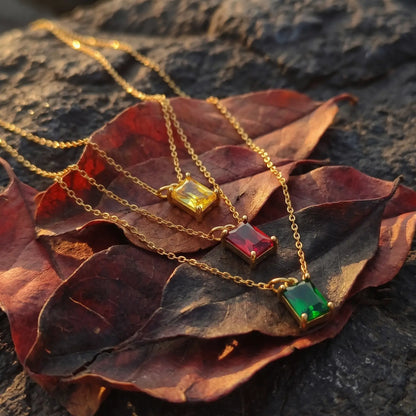Three rectangular birthstone pendant necklaces arranged on autumn leaves