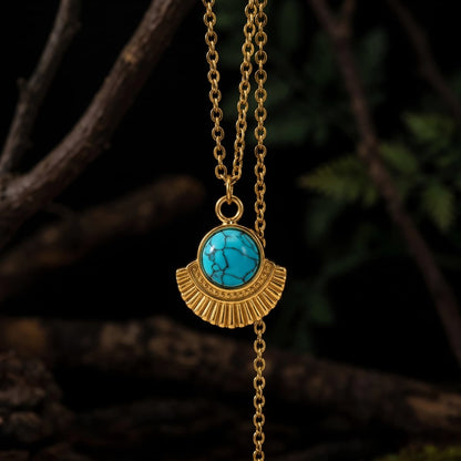 Oval natural turquoise pendant necklace with textured gold-tone frame on dark branches