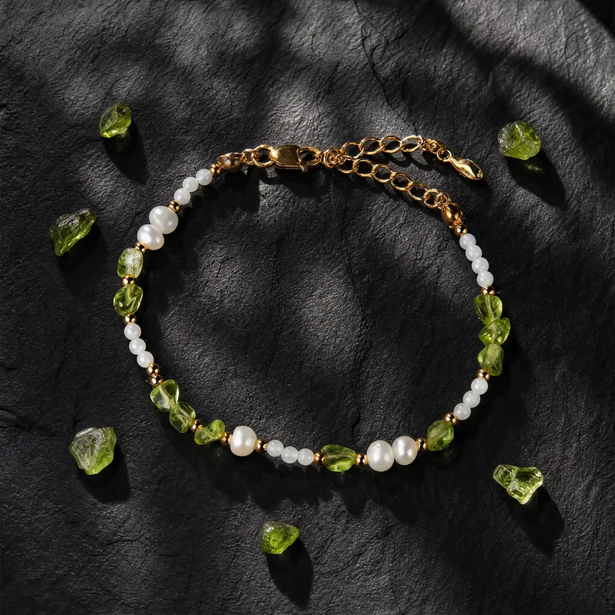 Peridot and pearl bracelet displayed on dark stone with loose green stones