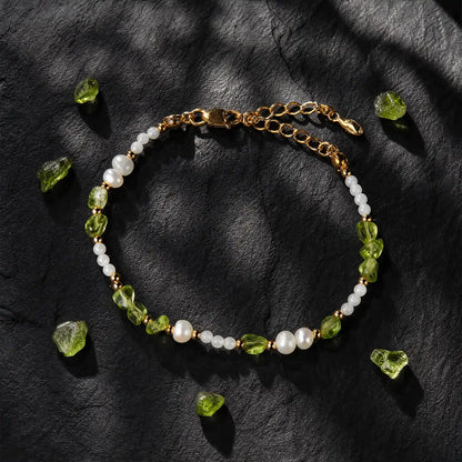 Peridot and pearl bracelet displayed on dark stone with loose green stones