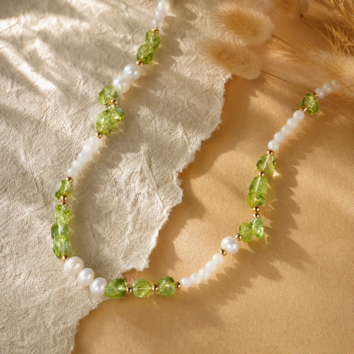 Peridot chip and pearl necklace arranged on warm cream fabric