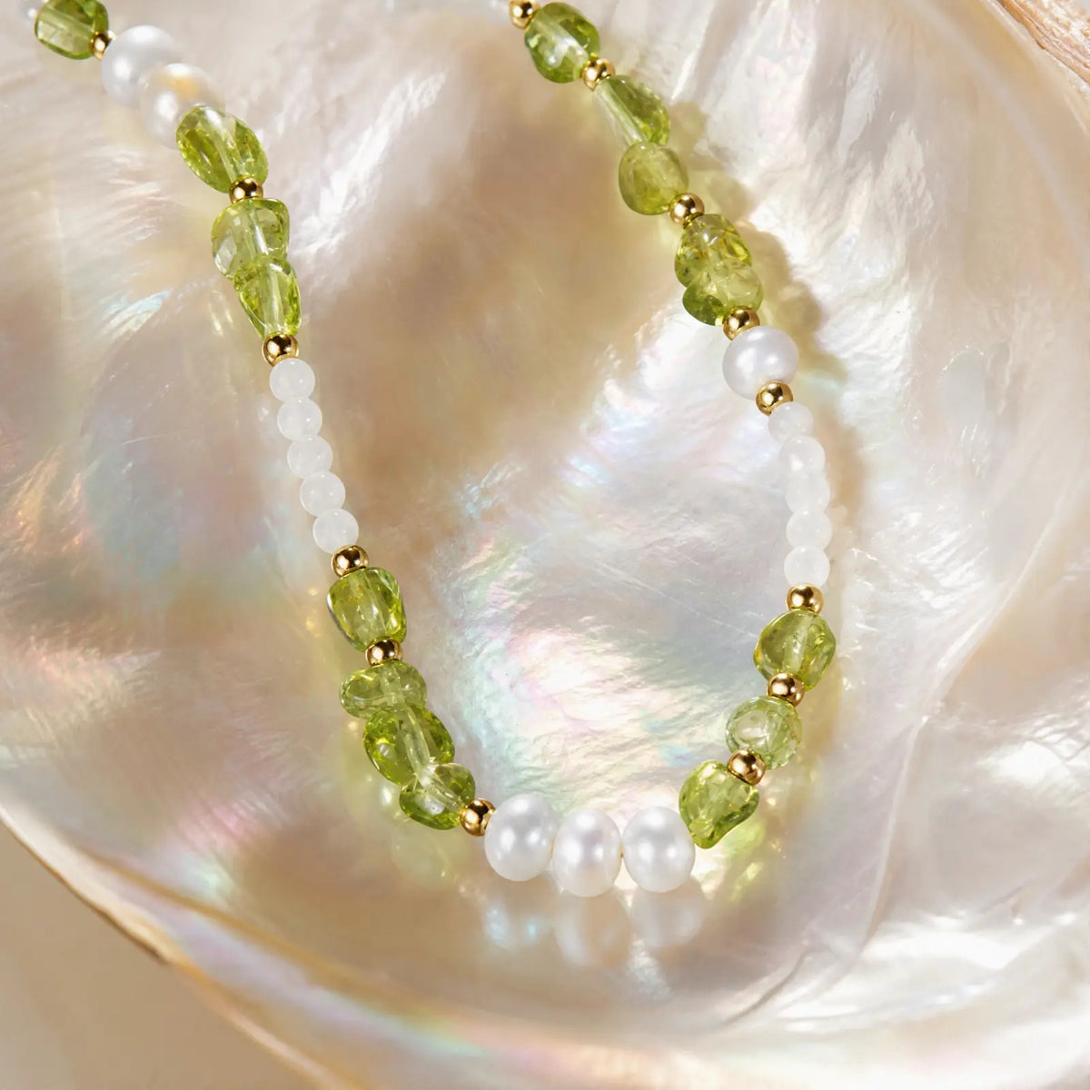 Peridot and pearl necklace displayed on an iridescent shell surface