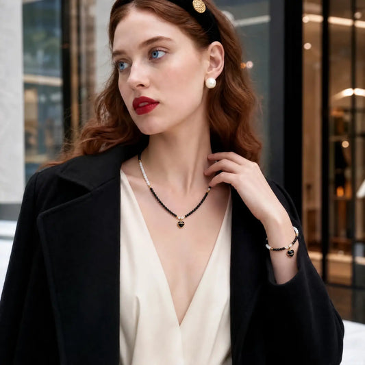 Woman wearing a black spinel and white shell bead necklace with a small onyx heart pendant