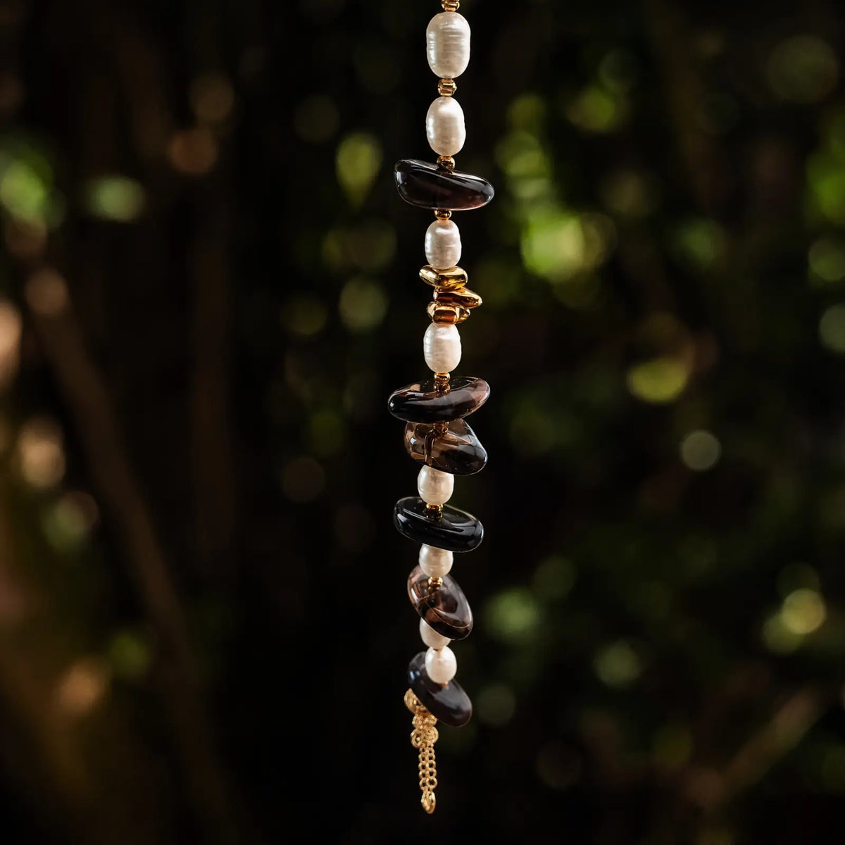 Smoky quartz and freshwater pearl bracelet hanging in a green natural setting