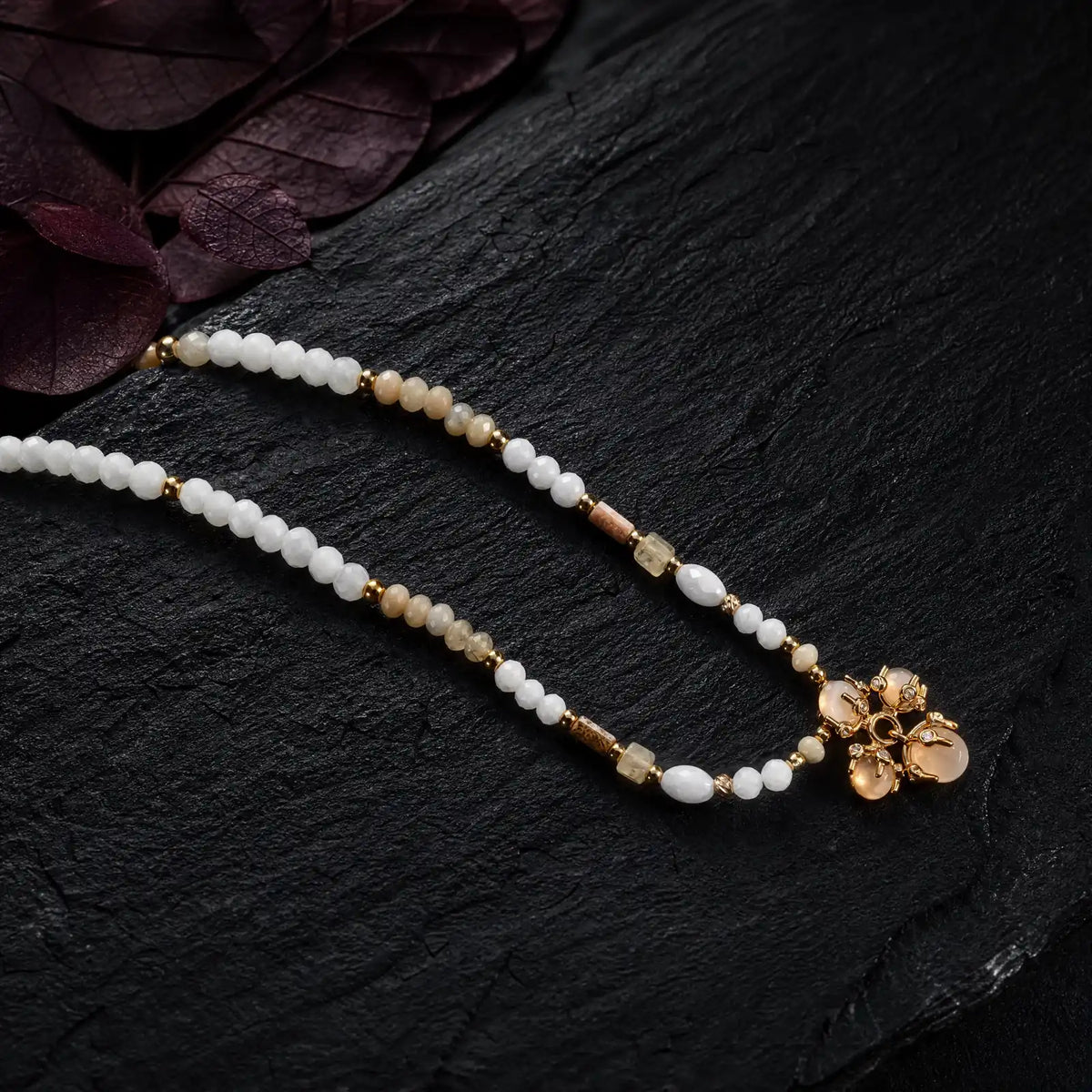 Close view of picture jasper shell beads and an opal cluster pendant on dark stone
