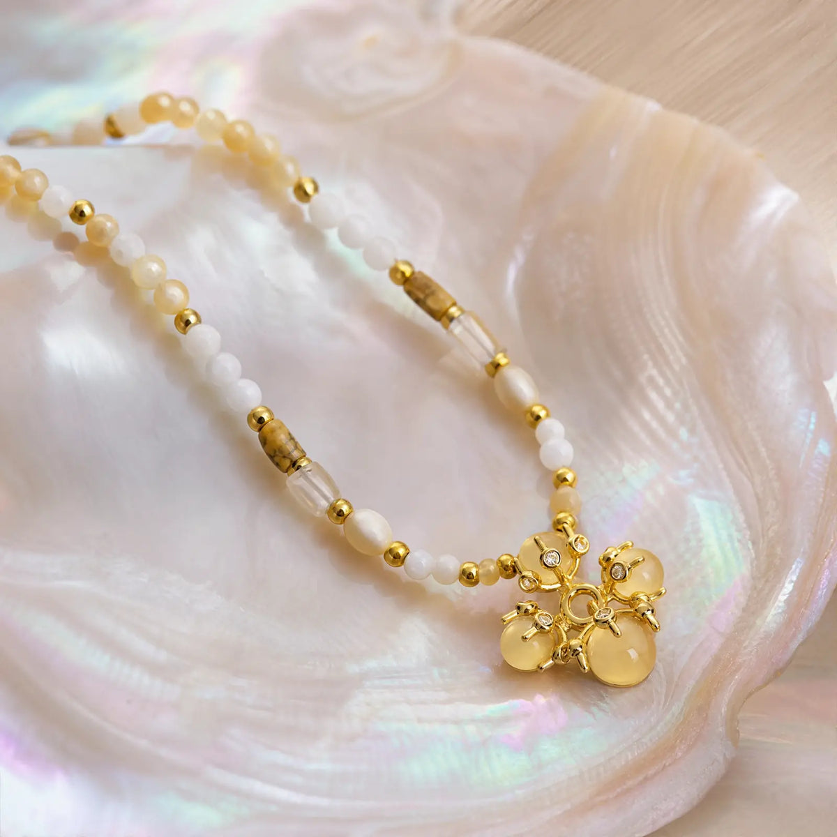 Opal bloom pendant and pale beaded strand displayed on an iridescent shell