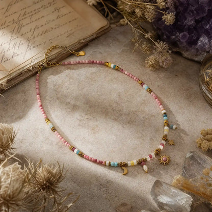 Rose-toned natural stone necklace with celestial charms on a light surface