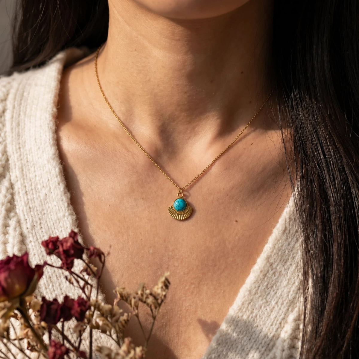 Round turquoise pendant necklace worn with a cream cardigan and flowers.
